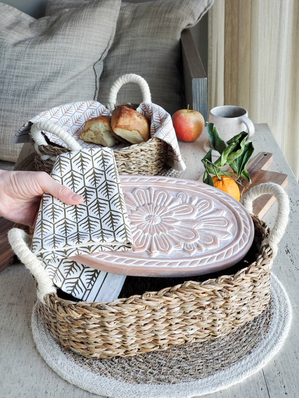 Woven basket with a ceramic dish, bread, and apples on a wooden surface.